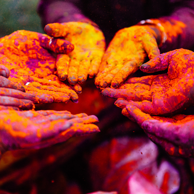 Tide and Seek sustainable swimwear blog post on spring destination to travel to including Holi in India - photo of hands covered in colourful powers that are thrown at the Holi festival