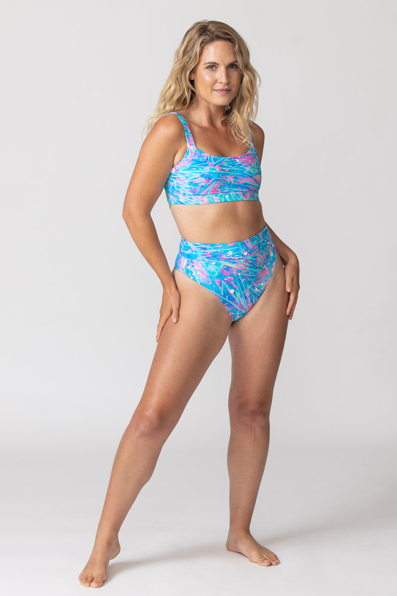 Tide and seek sustainable swimwear model wearing cosmic bolt blue and pink fitness bikini top and high waisted bikini bottoms full body image