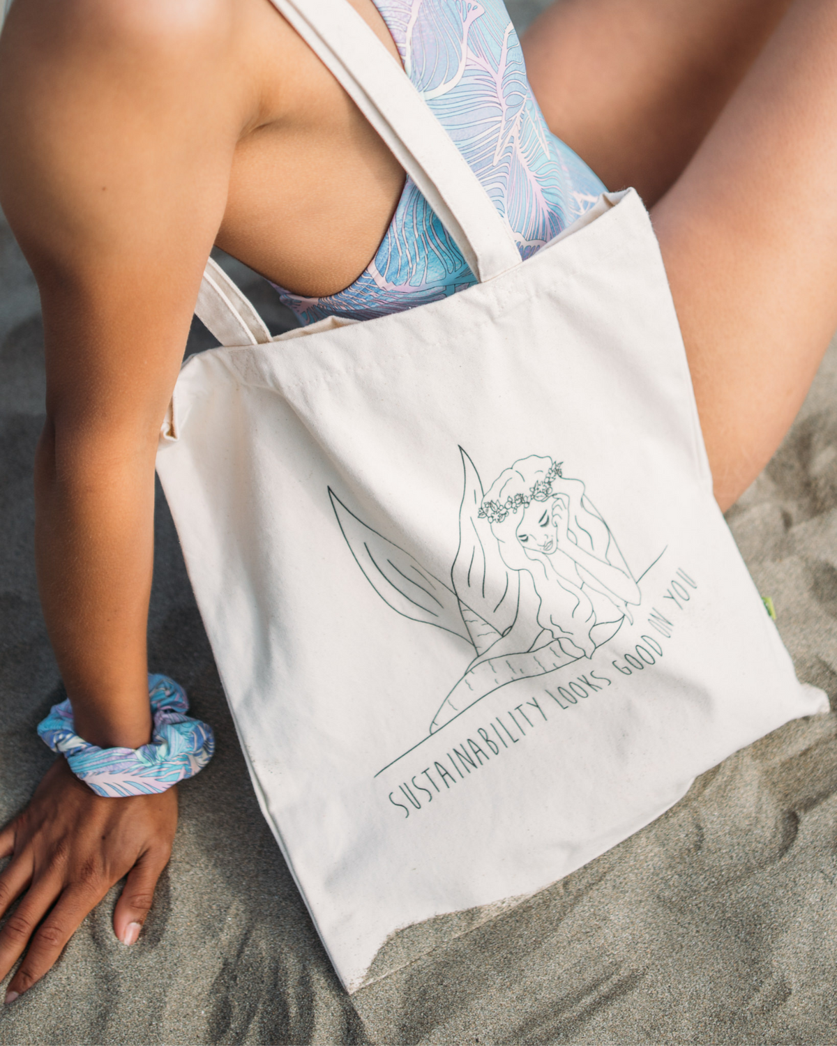 Tide and Seek Sustainable Swimwear tote bag on the beach worn by model with Tide + Seek slogan on the bag "Sustainability Looks Good On you". 