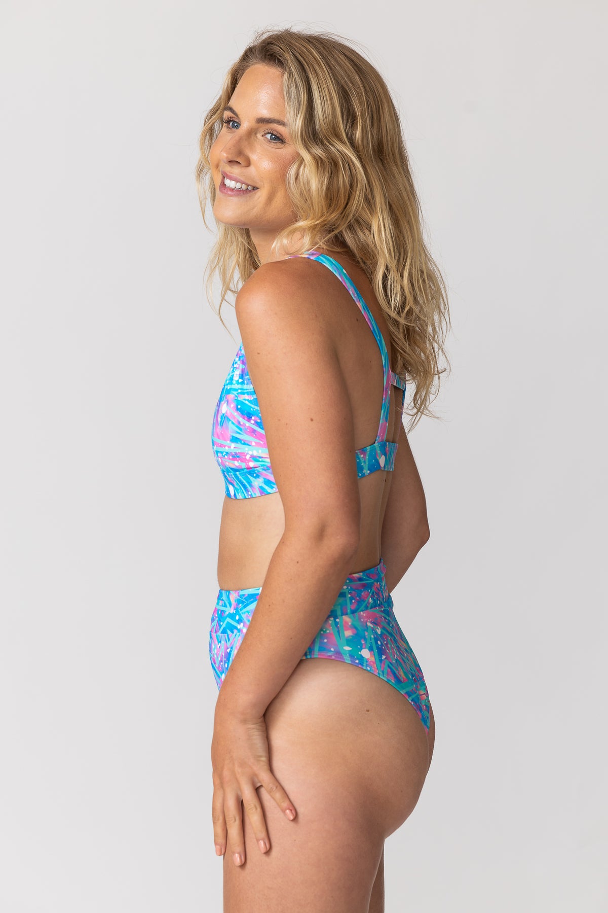 Tide and Seek sustainable swimwear blonde model wearing cosmic bolt pink and blue print triangle plunge bikini top and high waisted bikini bottoms 